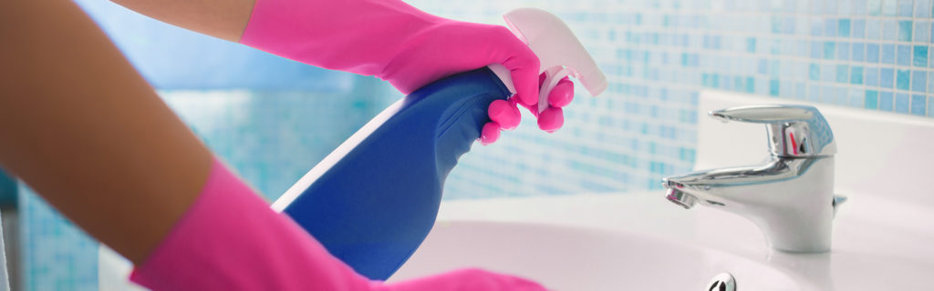 person with pink gloves spraying down bathroom sink with sanitizing spray